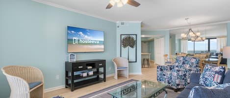 A living room with a television, wicker chairs, a glass coffee table, and a ceiling fan.