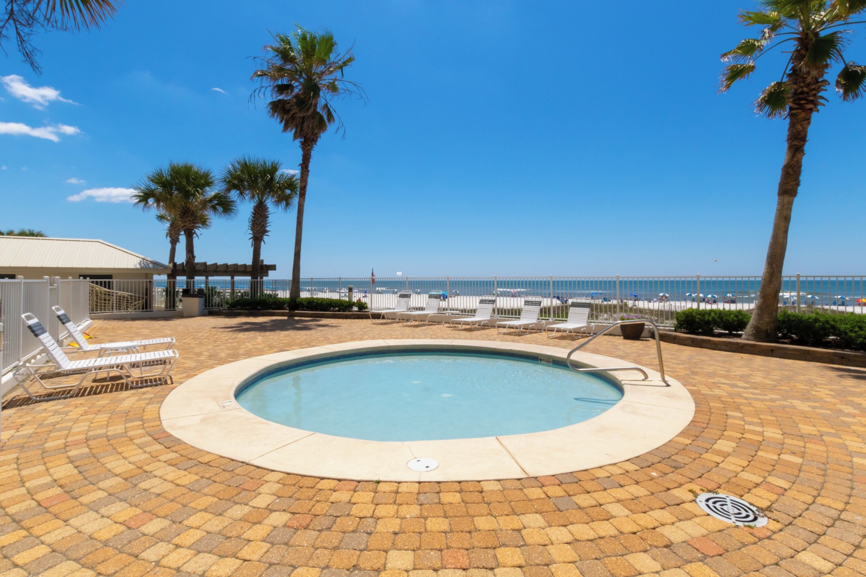 A pool area with lounge chairs and palm trees, overlooking a beach and ocean.