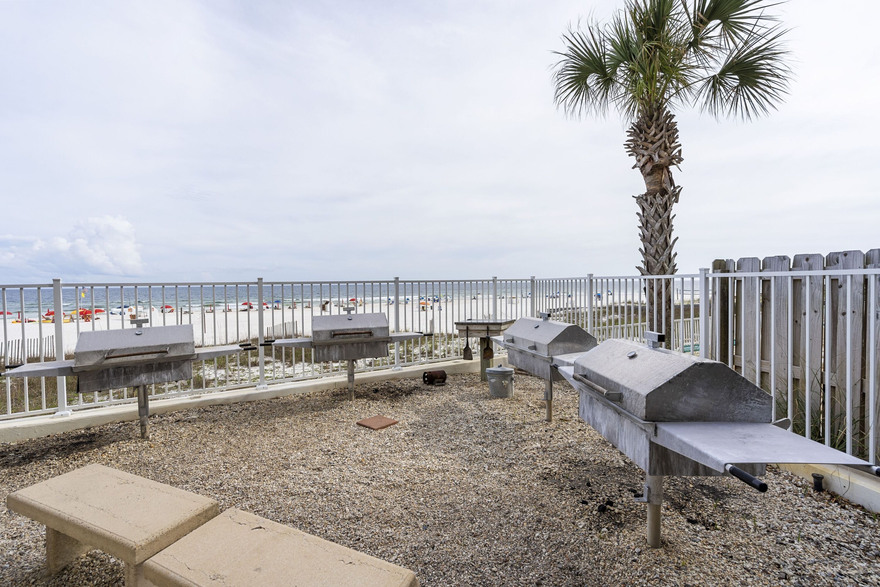 An outdoor patio with a grill, a bench, and a view of the beach.