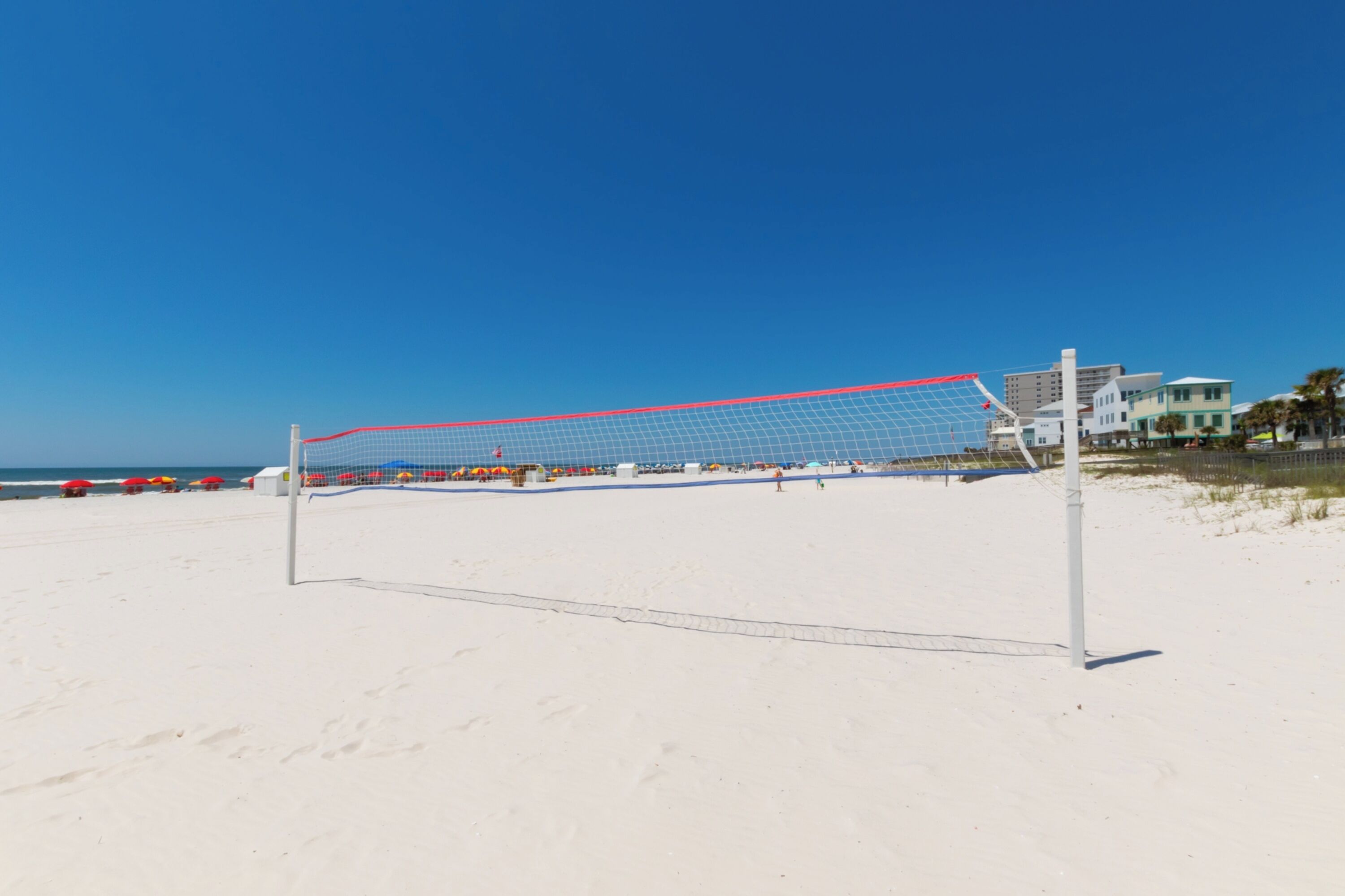 A beach volleyball net on a sandy beach with a clear blue sky.