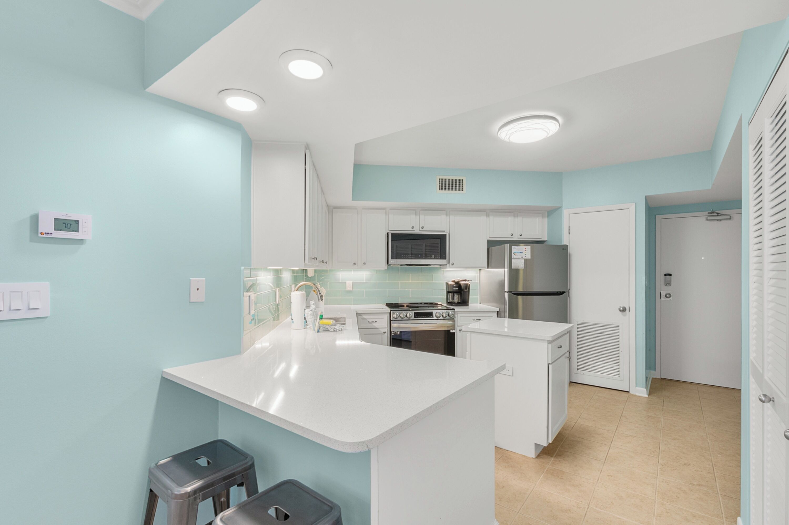 Une cuisine moderne avec des meubles blancs, un îlot central, des appareils en acier inoxydable et des spots encastrés au plafond.