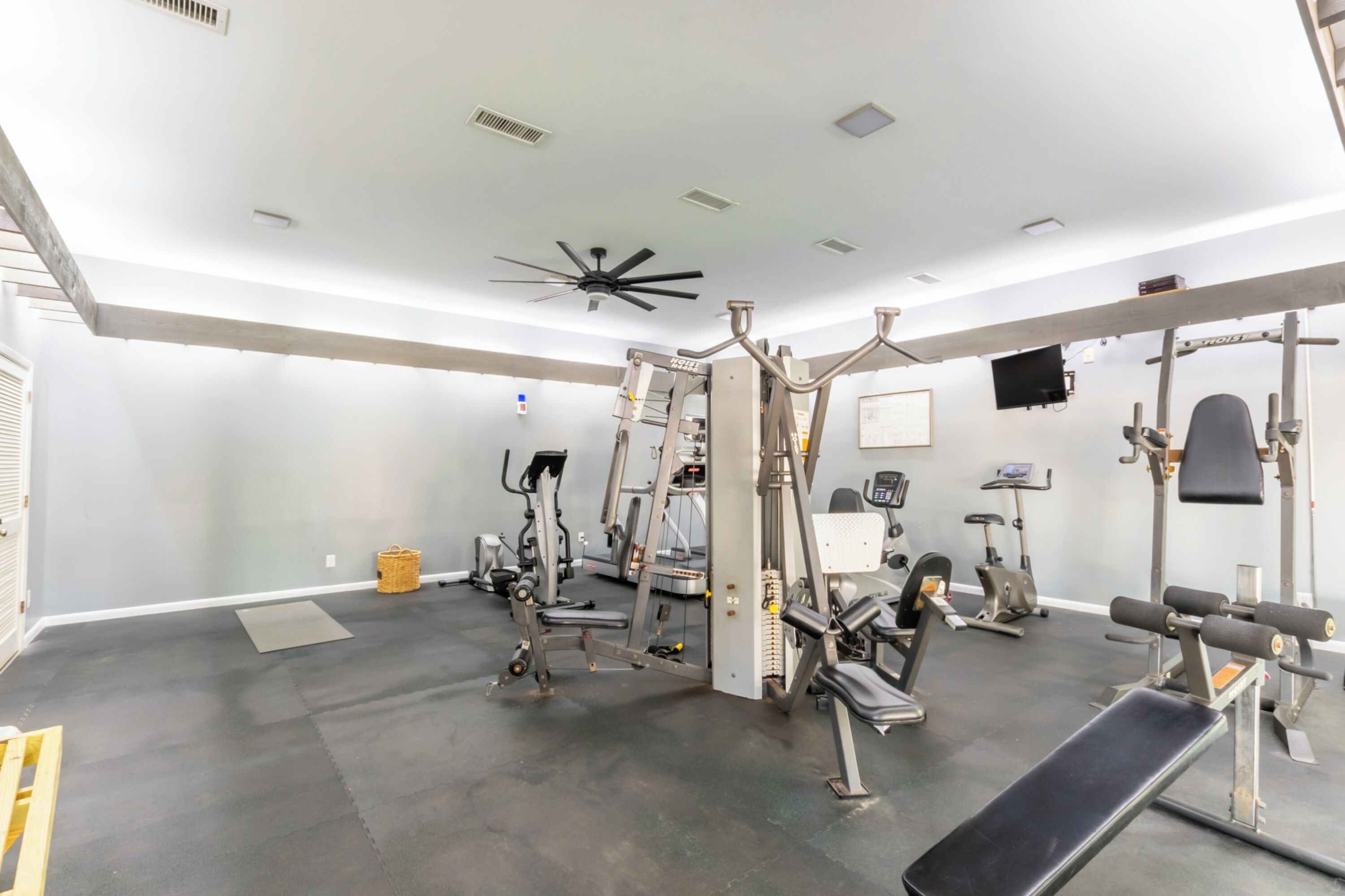 A gym with various exercise equipment, a ceiling fan, and a television on the wall.
