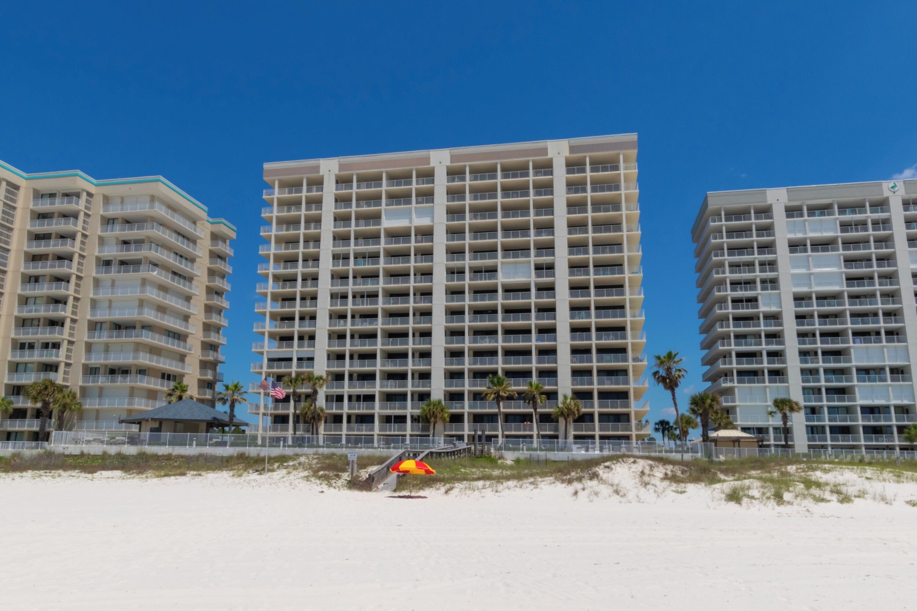 A beachfront hotel with multiple floors, balconies, and a sandy beach in the foreground.