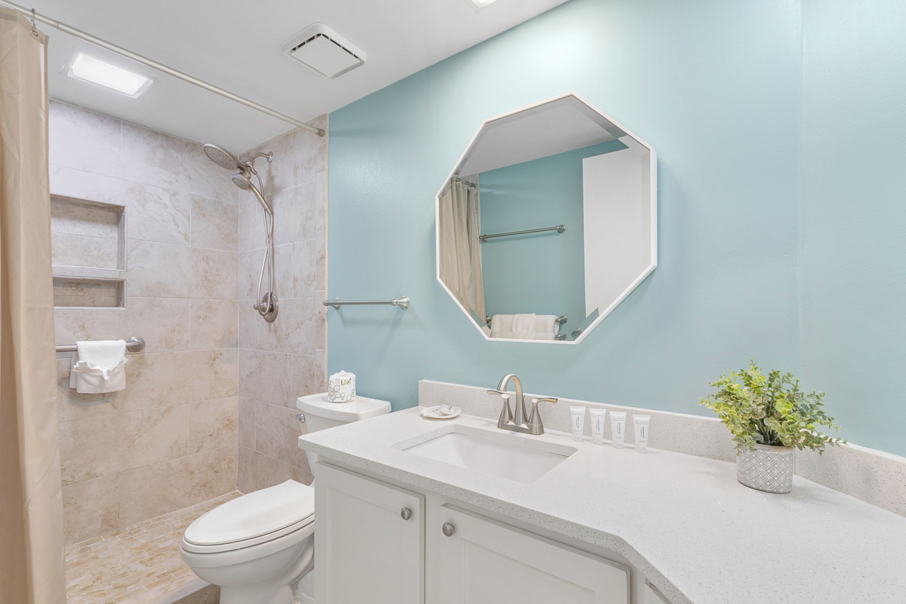 A bathroom with a shower, toilet, sink, and mirror.