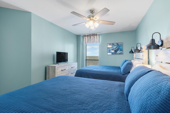A bedroom with two beds, a ceiling fan, a TV, and a window with blinds. - Windward Pointe 803 (Orange Beach)