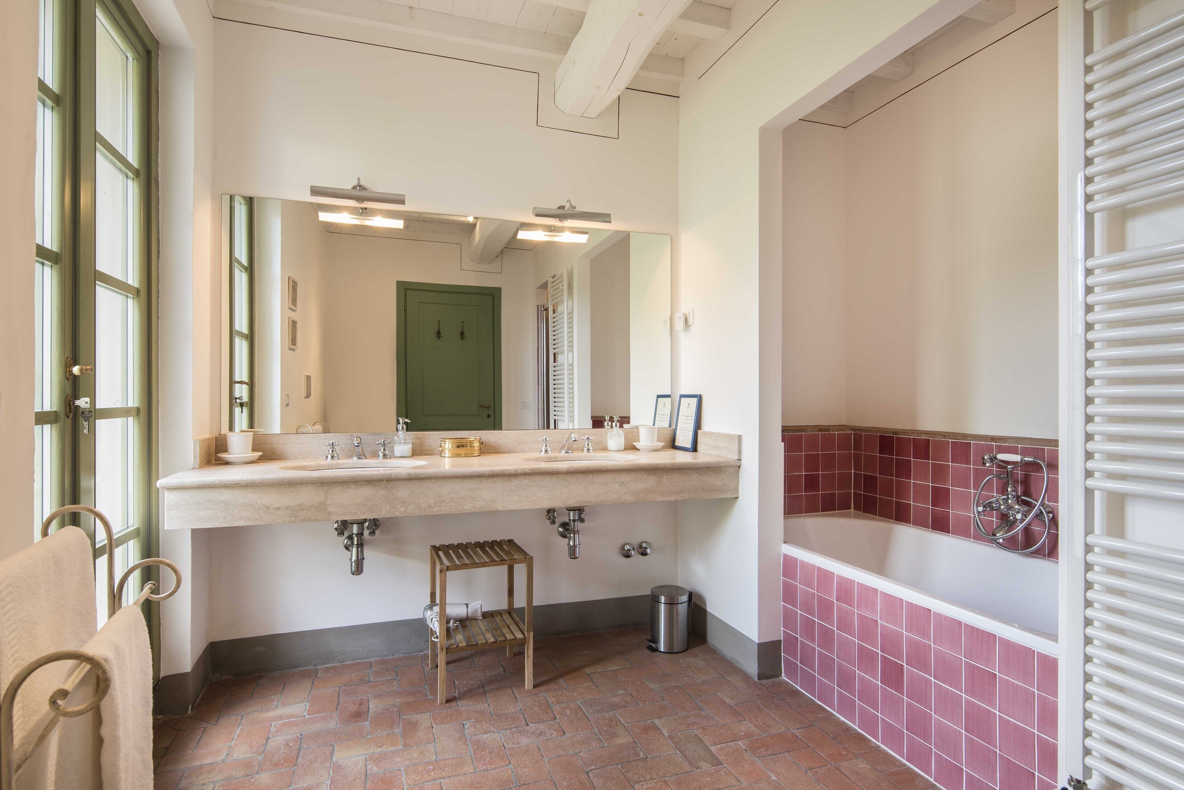 A bathroom with a large sink, a mirror, a green door, and a tiled floor.
