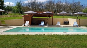 Une piscine entourée de chaises longues et de parasols, ainsi que d’une pergola en bois et d’une pelouse.