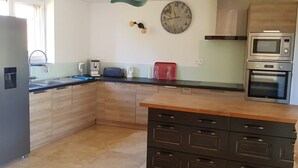A modern kitchen with a wooden countertop, built-in cabinets, a sink, a clock, a microwave, and an oven. - La Truffière (Pays-de-Belvès)