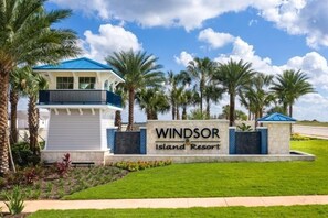 A sign for Windsor Island Resort with a view of the resort's exterior, including a building with a blue roof and palm trees.