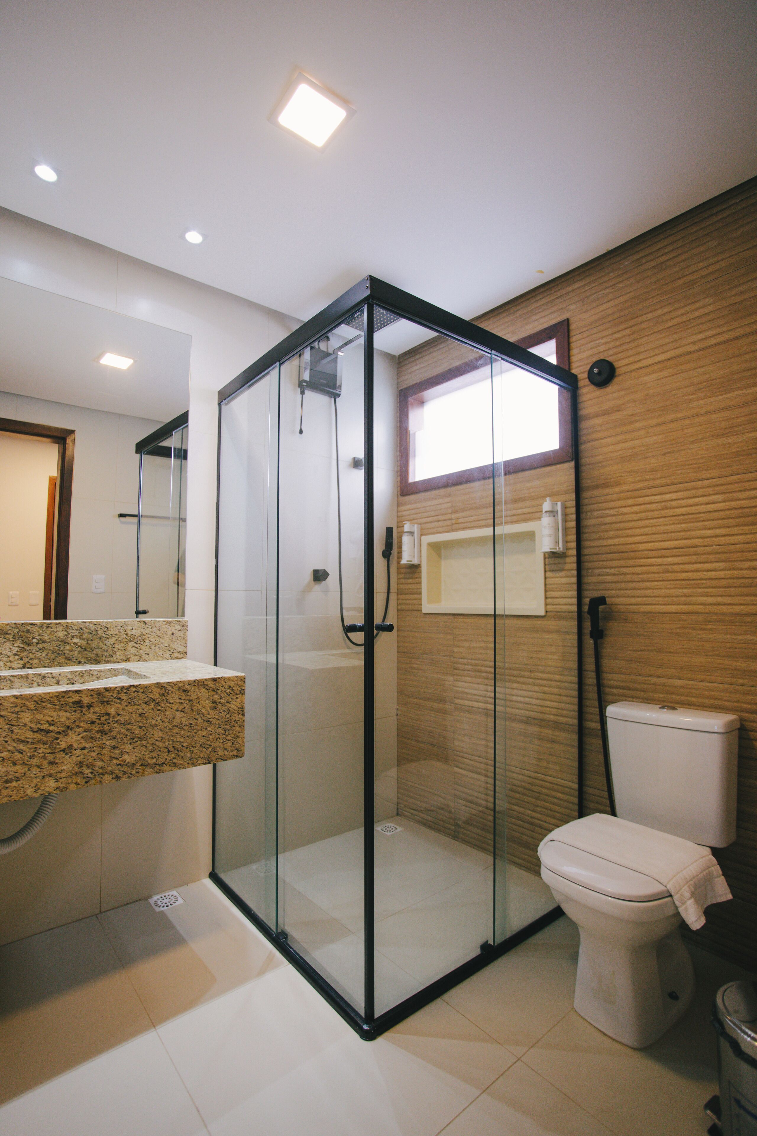 A modern bathroom with a glass-enclosed shower, a toilet, and a granite countertop.