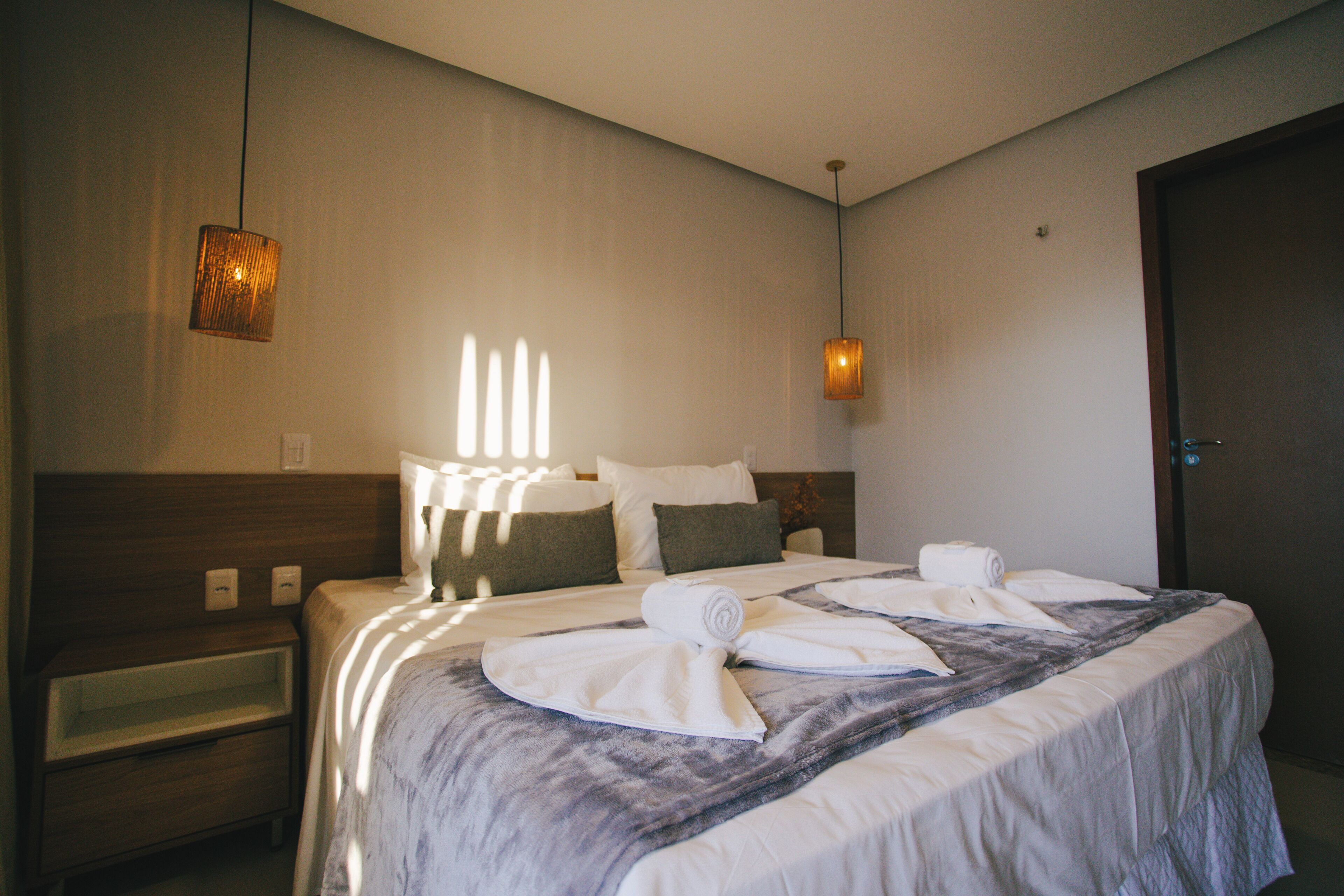 A neatly made bed with towels, a bedside table, and a wall-mounted lamp.