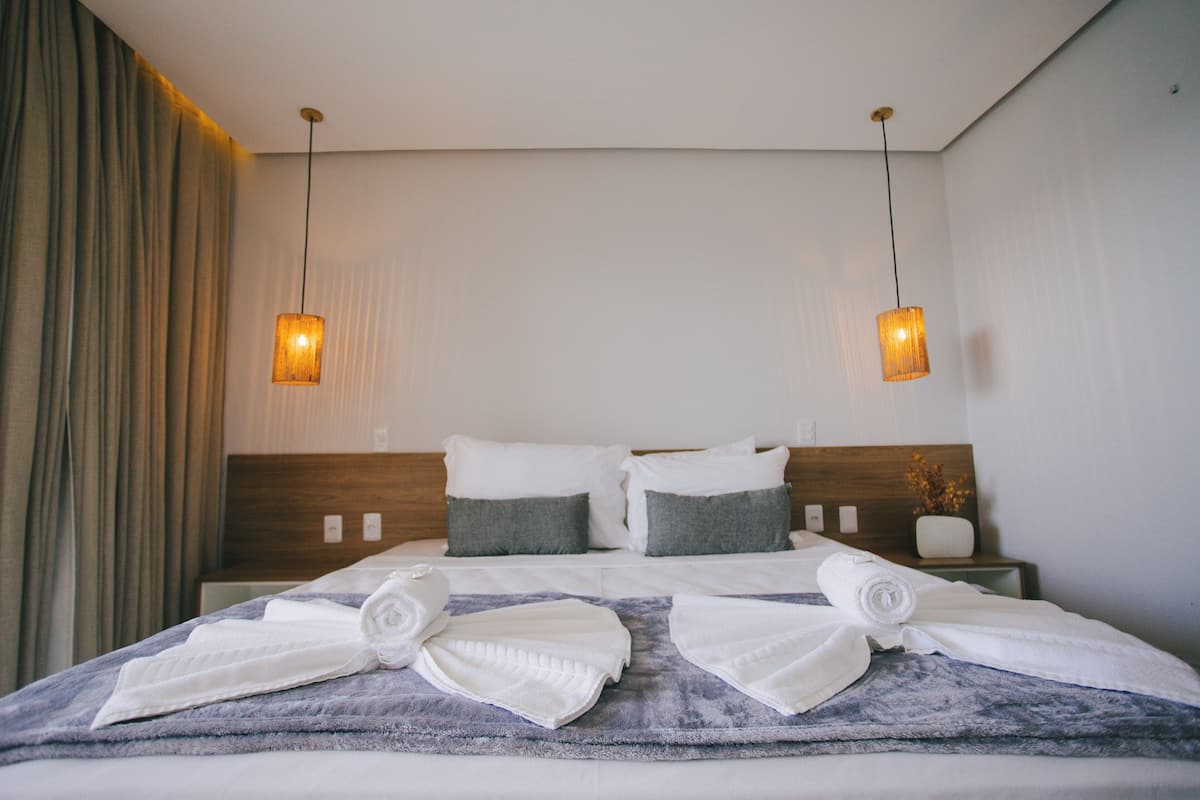 Une chambre d’hôtel avec un lit bien fait, deux lampes de chevet et une table de chevet ornée d’un vase de fleurs.