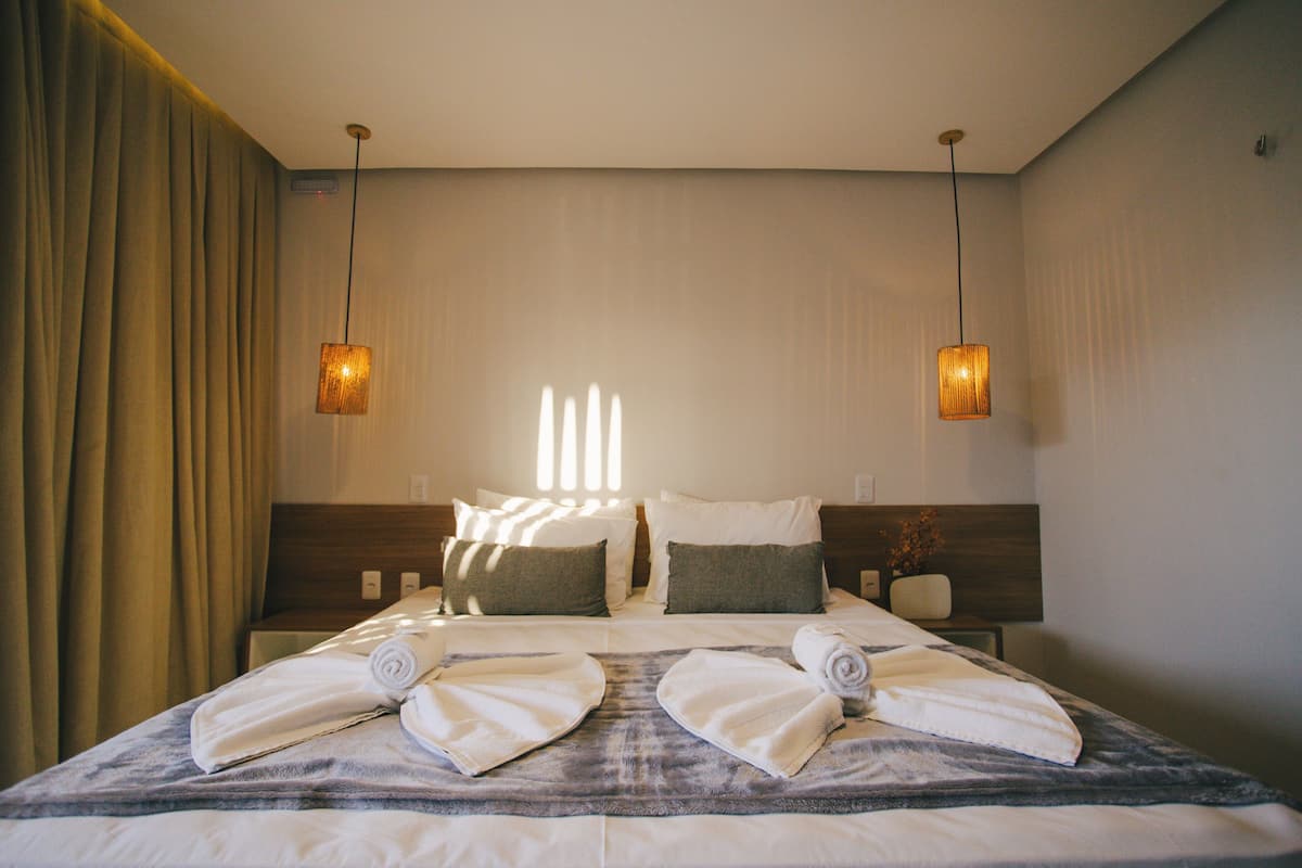 Une chambre d’hôtel avec un lit bien fait, deux tables de chevet et deux lampes suspendues.