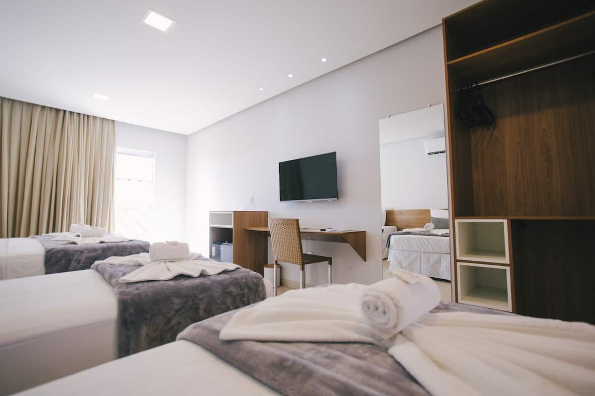 Une chambre d’hôtel avec trois lits, un bureau, une télévision et une armoire.
