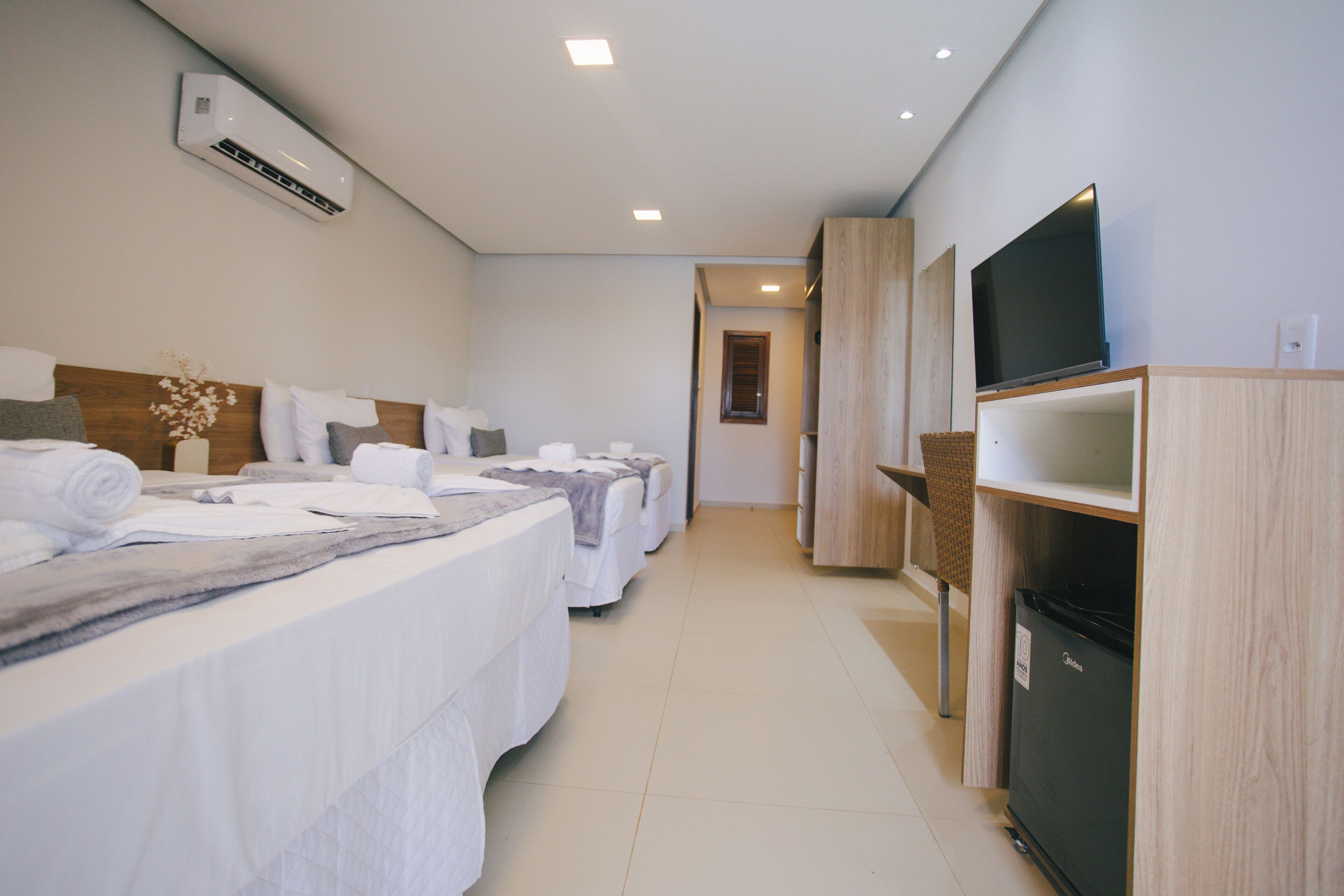 A hotel room with two beds, a television, a refrigerator, and an air conditioning unit.