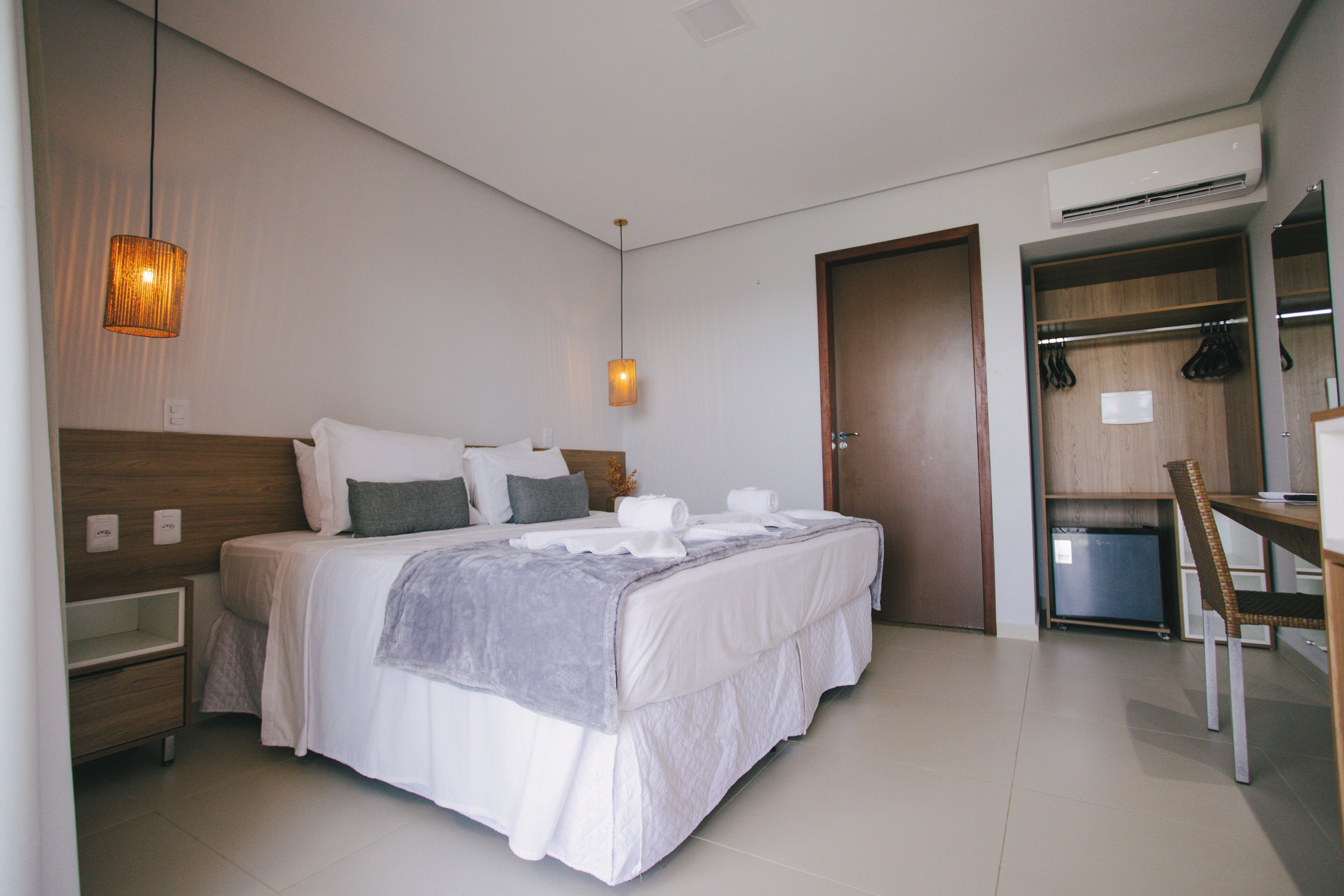 A modern hotel room with a neatly made bed, a bedside table, a desk, and a wardrobe.