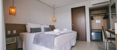 A modern hotel room with a neatly made bed, a bedside table, a desk, and a wardrobe.