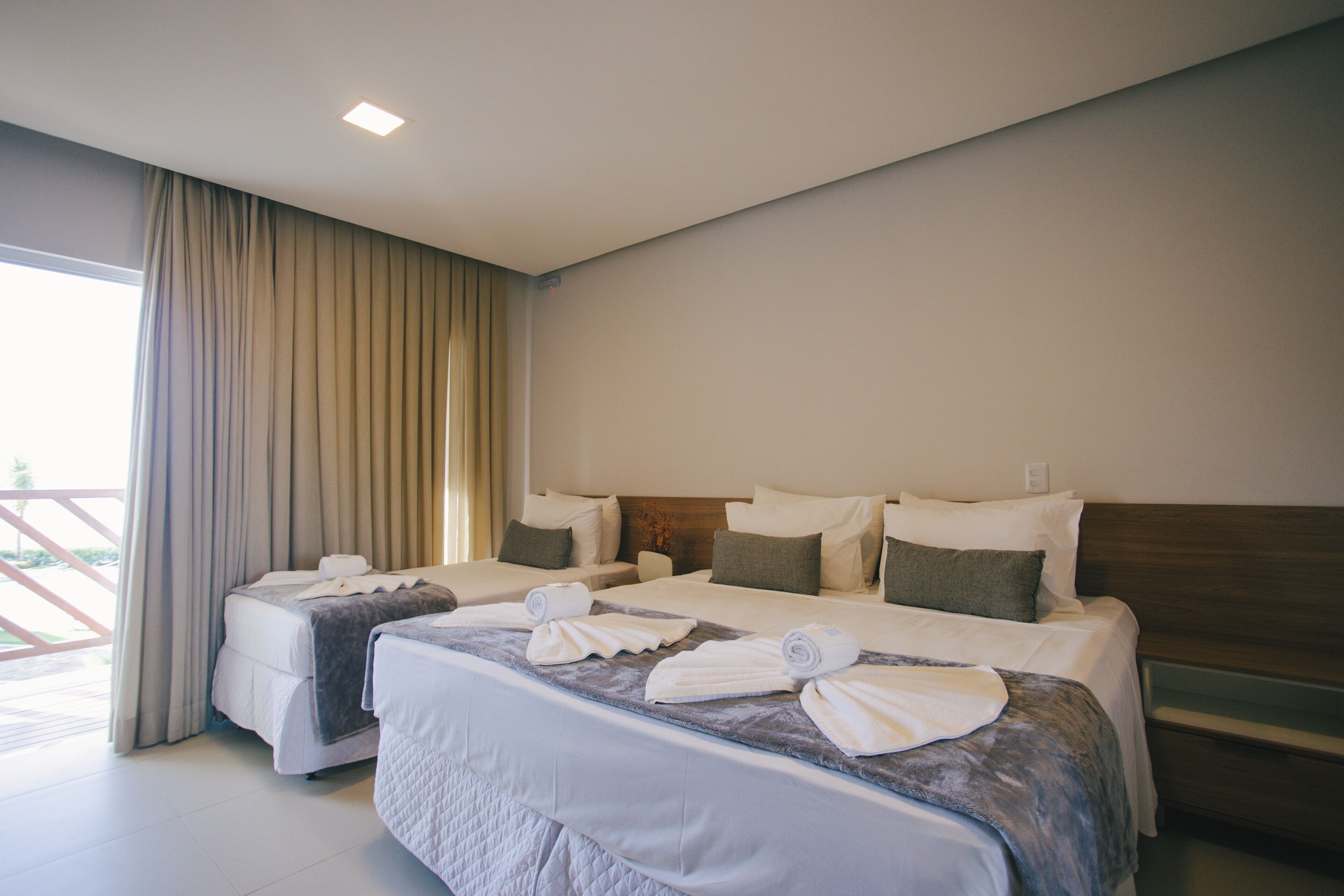 A hotel room with two beds, a large window with curtains, and a view of the outdoors.