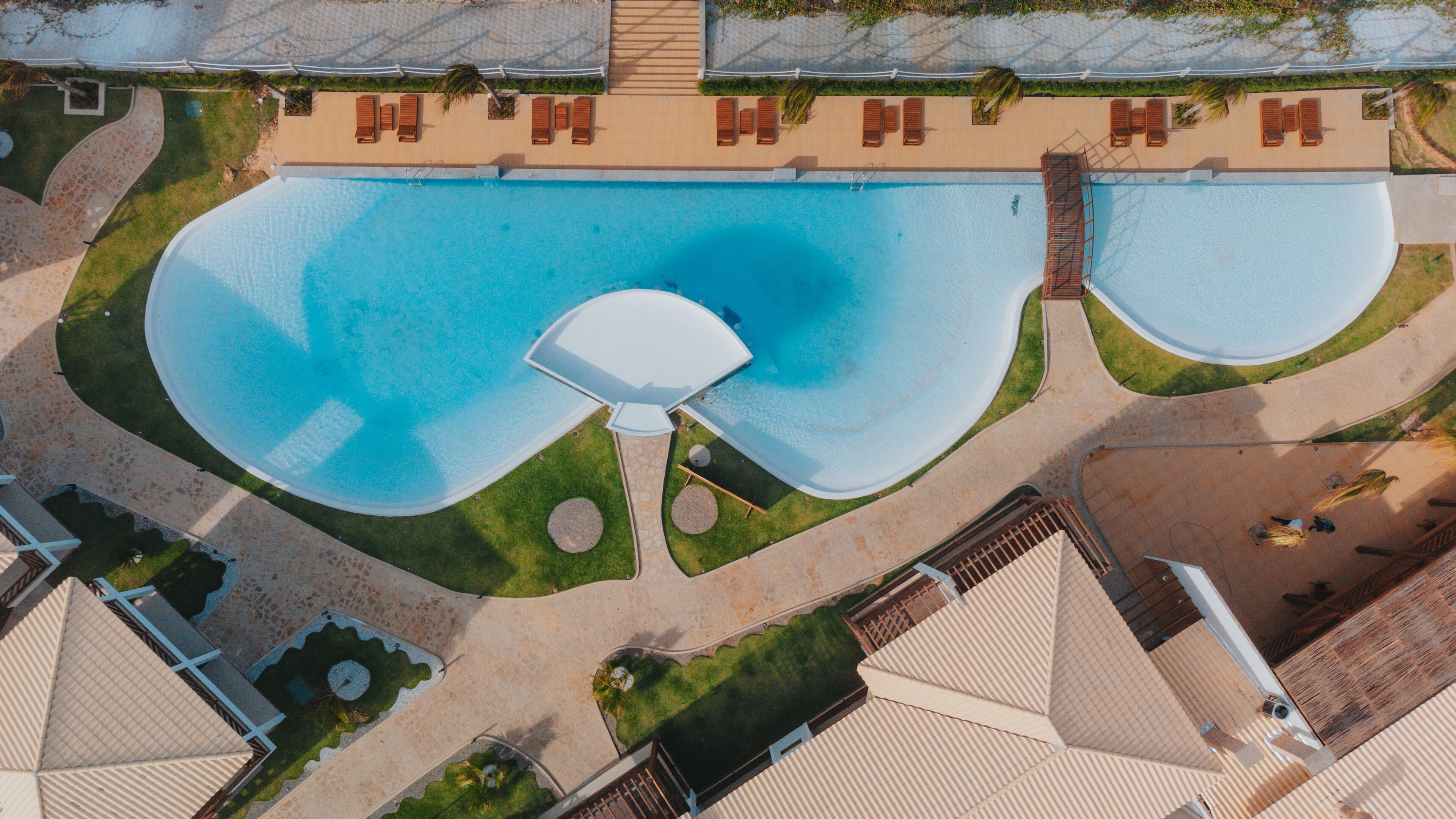 An aerial view of a resort with a large central pool, multiple lounge areas, and a well-maintained landscape.