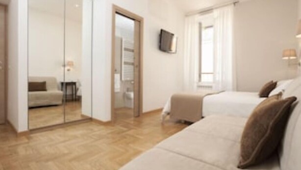 A hotel room with a wooden floor, a sofa bed, a TV mounted on the wall, and a door leading to another room. - DIMORA VATICAN apartment's Dx (Roma)
