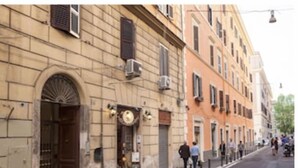 A street view with a building featuring a large arched entrance, multiple windows, and air conditioning units. - DIMORA VATICAN apartment's Dx (Roma)