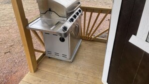 Een draagbare gasgrill op een houten terras, met uitzicht op een droog landschap.