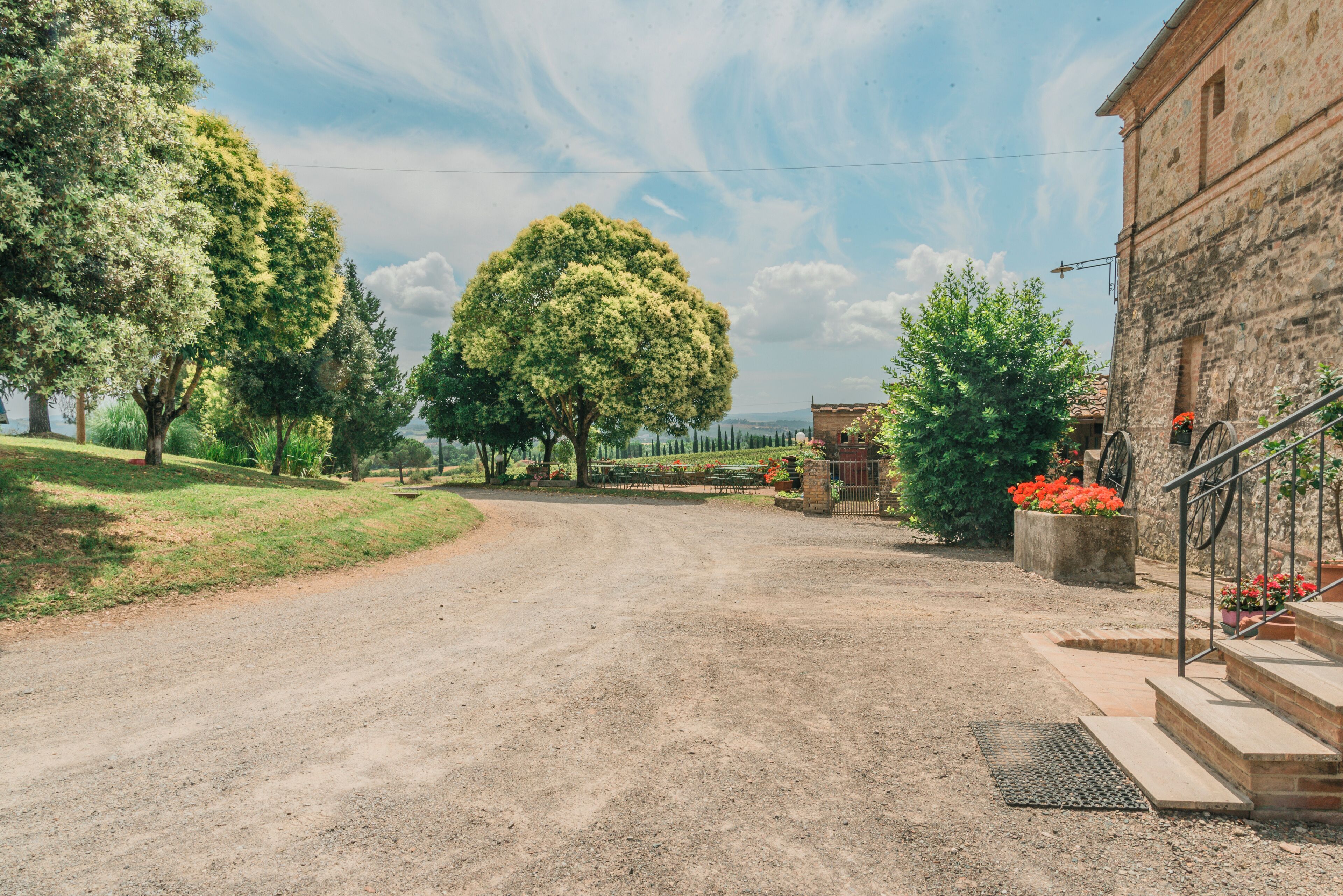 Un camino rural que lleva a un edificio de piedra con jardín y escalones.