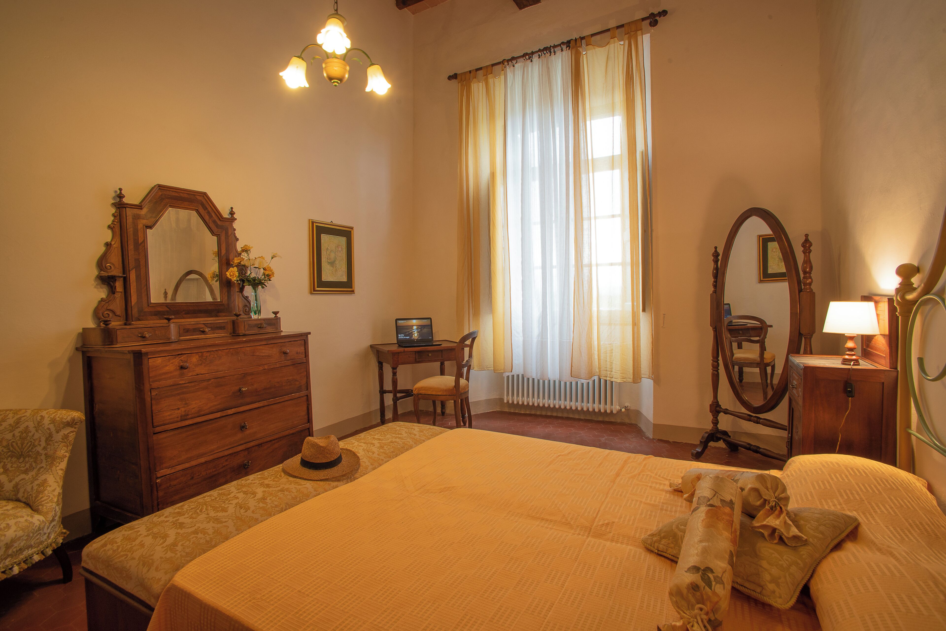 Une chambre à coucher avec un grand lit, une commode, une chaise, un bureau avec un ordinateur portable et une fenêtre avec des rideaux.