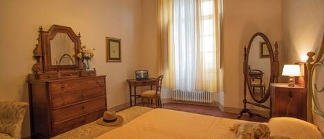 Une chambre à coucher avec un grand lit, une commode, une chaise, un bureau avec un ordinateur portable et une fenêtre avec des rideaux.