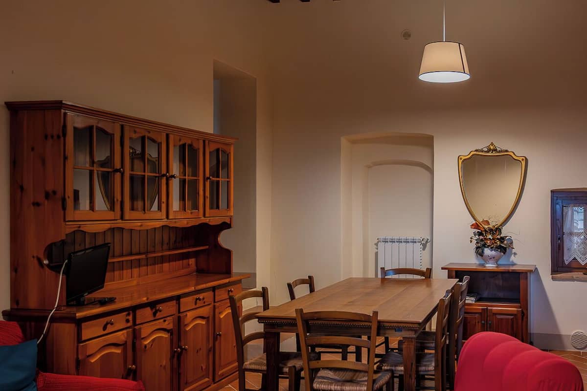 A dining area with a wooden table and chairs, a red armchair, and a wooden cabinet with glass doors.