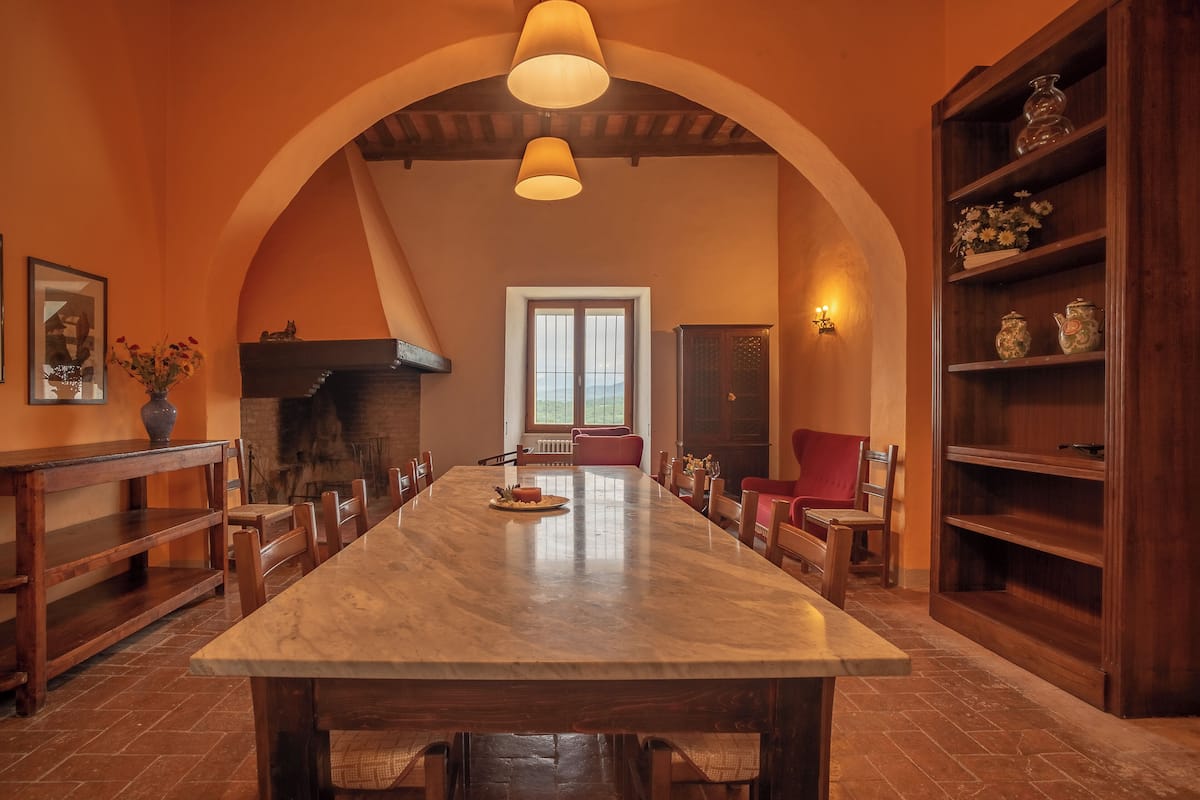 A spacious dining area with a large marble table, wooden chairs, and a fireplace.