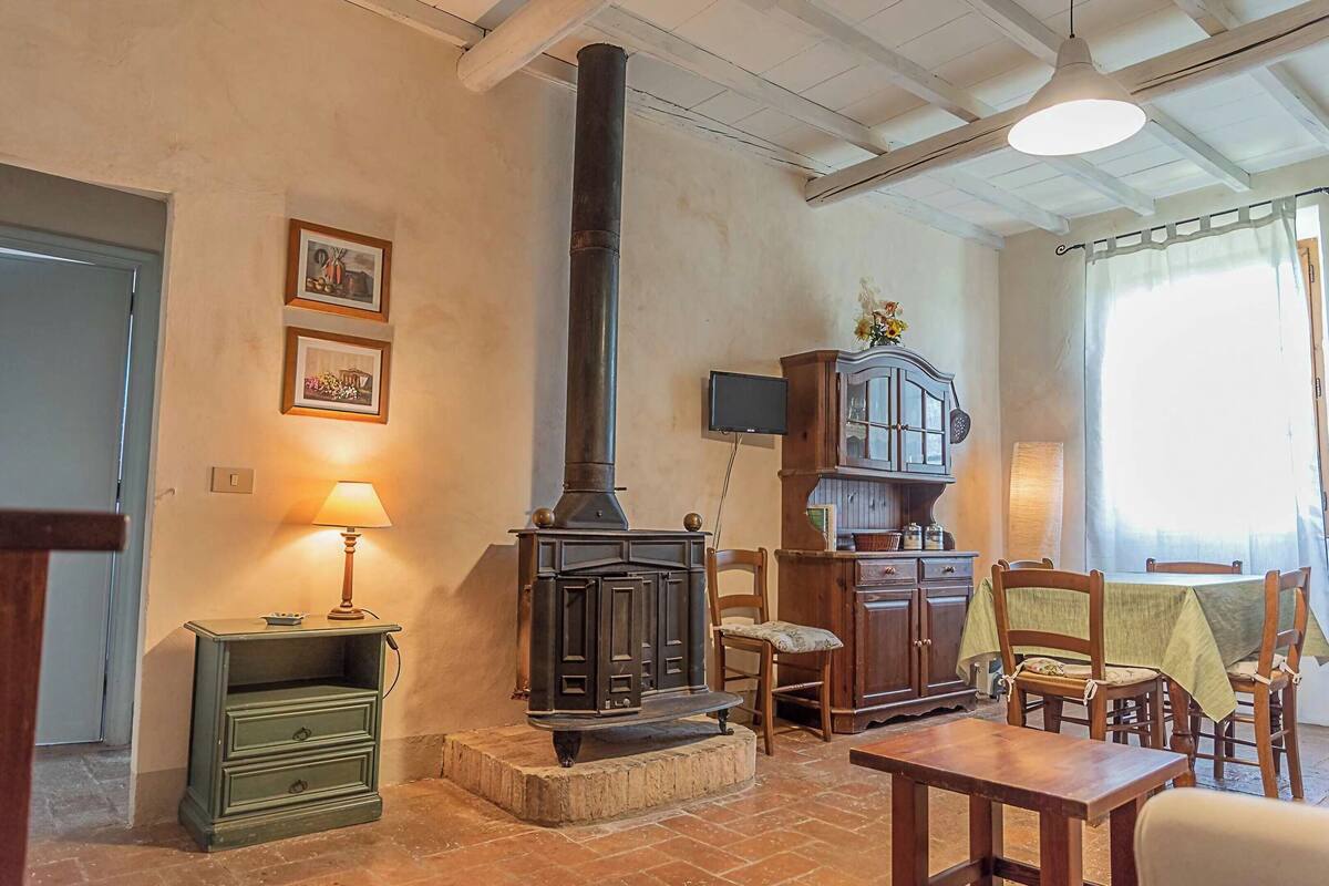 A cozy room with a wood-burning stove, a green nightstand, a wooden cabinet, and a dining table with chairs.