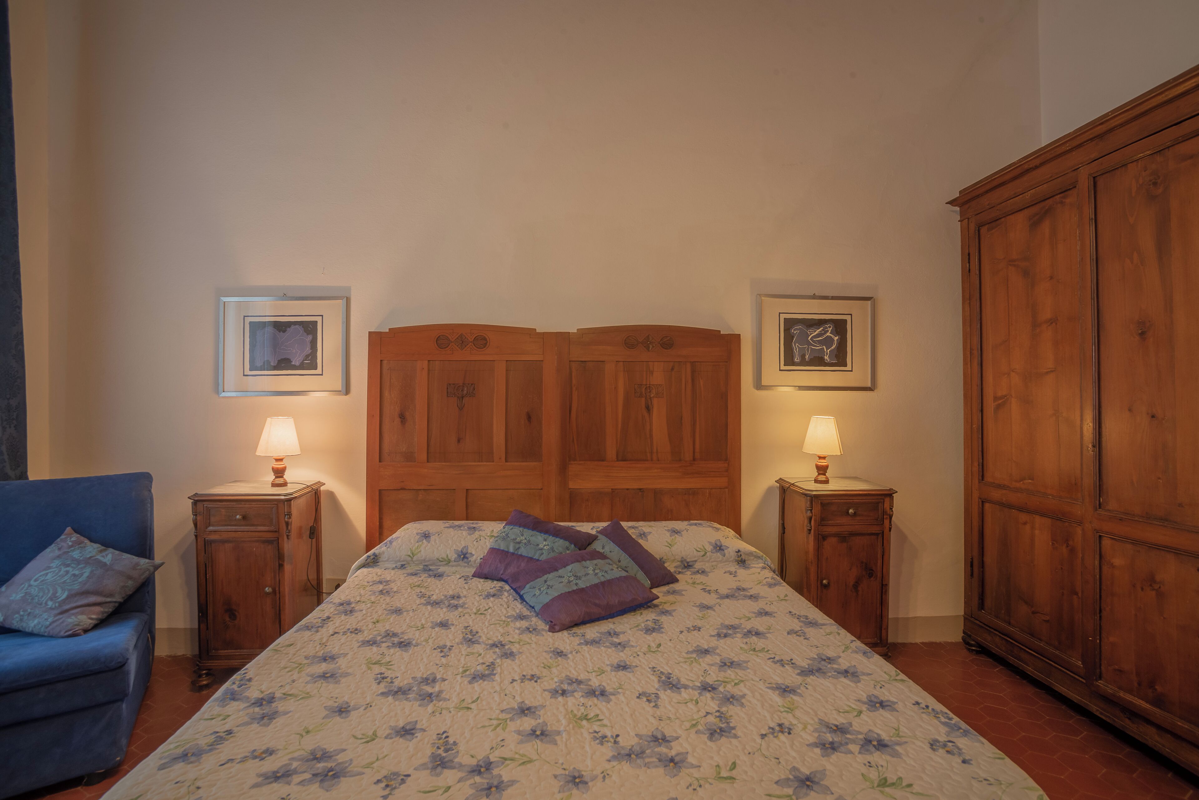 A bedroom with a large bed, two nightstands, a wooden wardrobe, and a blue armchair.