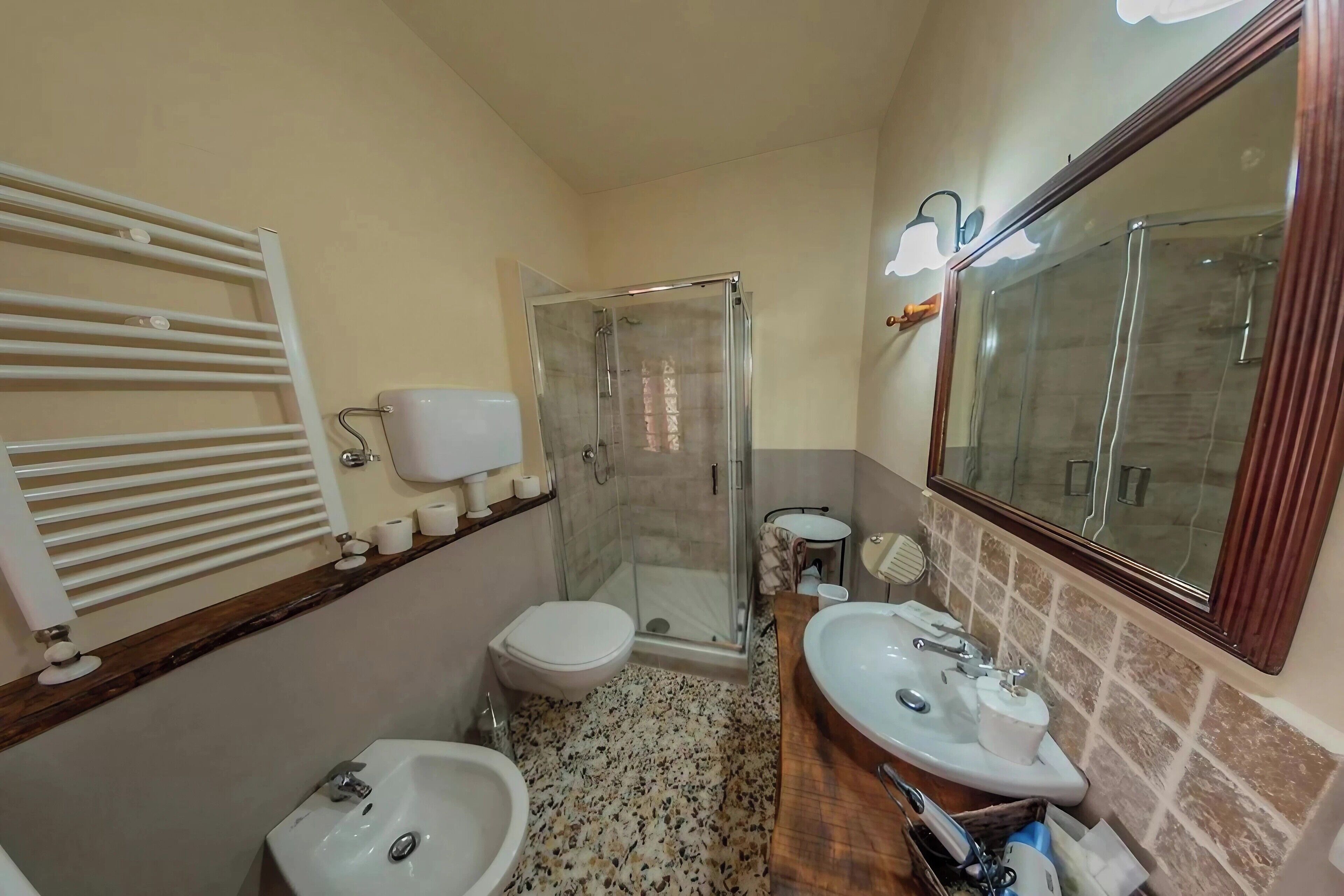 Un baño con ducha, inodoro, dos lavamanos y un espejo.