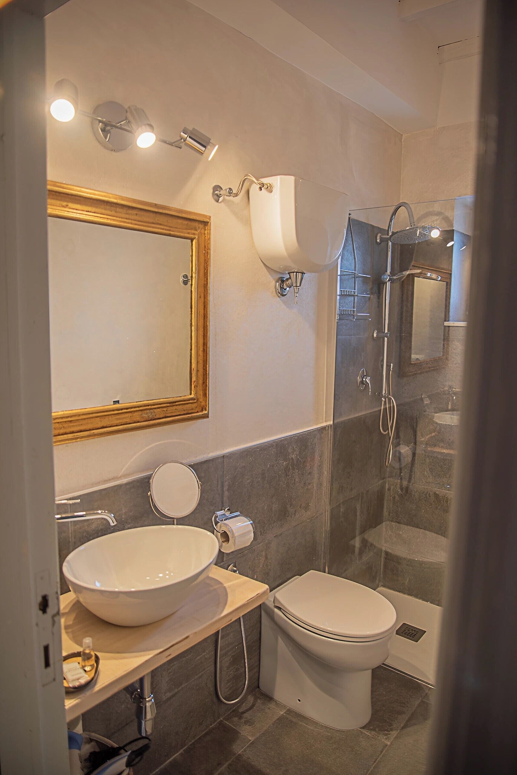 A modern bathroom with a large mirror, a vessel sink, a toilet, and a glass-enclosed shower area.