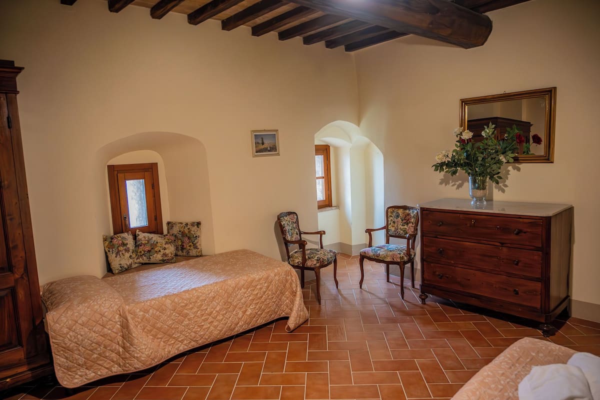 A bedroom with a bed, two chairs, a dresser, and a mirror.