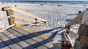 En trätrappa som leder ner till en sandstrand med fri utsikt över havet.