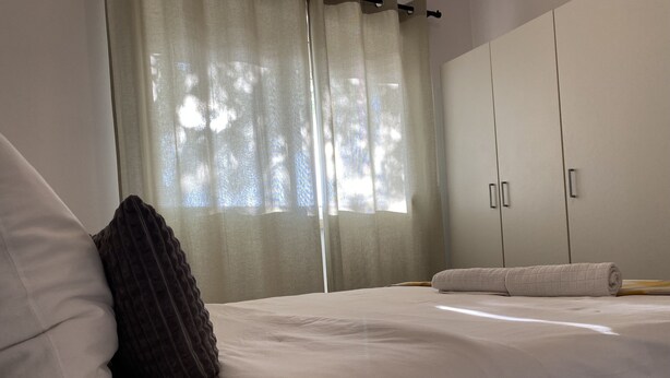 Une chambre à coucher avec un lit, un oreiller marron foncé, un oreiller blanc et une serviette enroulée sur le lit. On y trouve également une armoire à deux portes et un miroir.