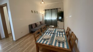 Un coin repas avec une table dressée pour quatre personnes, un canapé et un téléviseur posé sur un meuble.