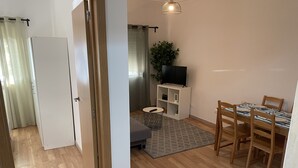 Un salon moderne comprenant un coin repas, un plancher en bois, un téléviseur posé sur un meuble blanc et une plante en pot.