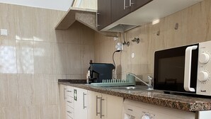 Une cuisine compacte équipée d’un lave-linge, d’un four à micro-ondes et d’une machine à café posée sur le plan de travail.