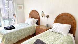 A room with two beds, each with a green floral bedspread and white pillows. There is a nightstand with a lamp and a small table between the beds. - Waterfront 2 BR cottage on 1 acre private lot walking distance to beaches! (Stanhope)
