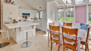 A modern kitchen with white cabinets, a central island, and a dining area with a table and chairs. - Waterfront 2 BR cottage on 1 acre private lot walking distance to beaches! (Stanhope)