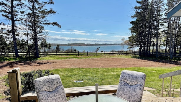 A deck with two chairs and a table, overlooking a lake and a fenced field. - Waterfront 2 BR cottage on 1 acre private lot walking distance to beaches! (Stanhope)