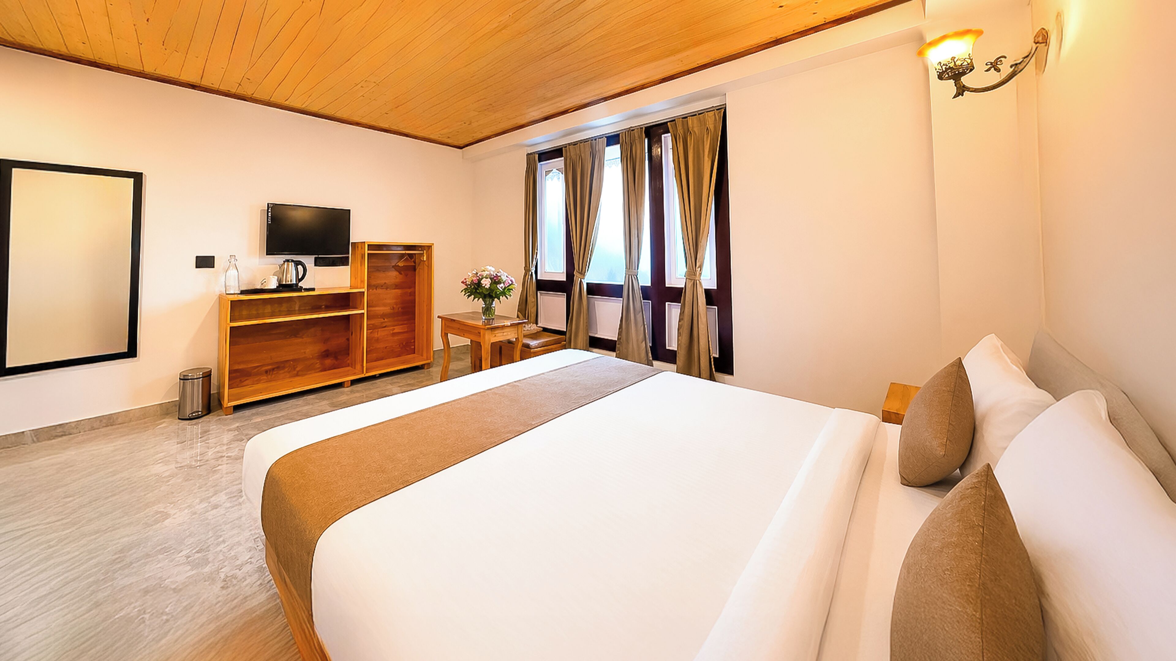 Een hotelkamer met een groot bed, houten meubels, een televisie en een raam met gordijnen.