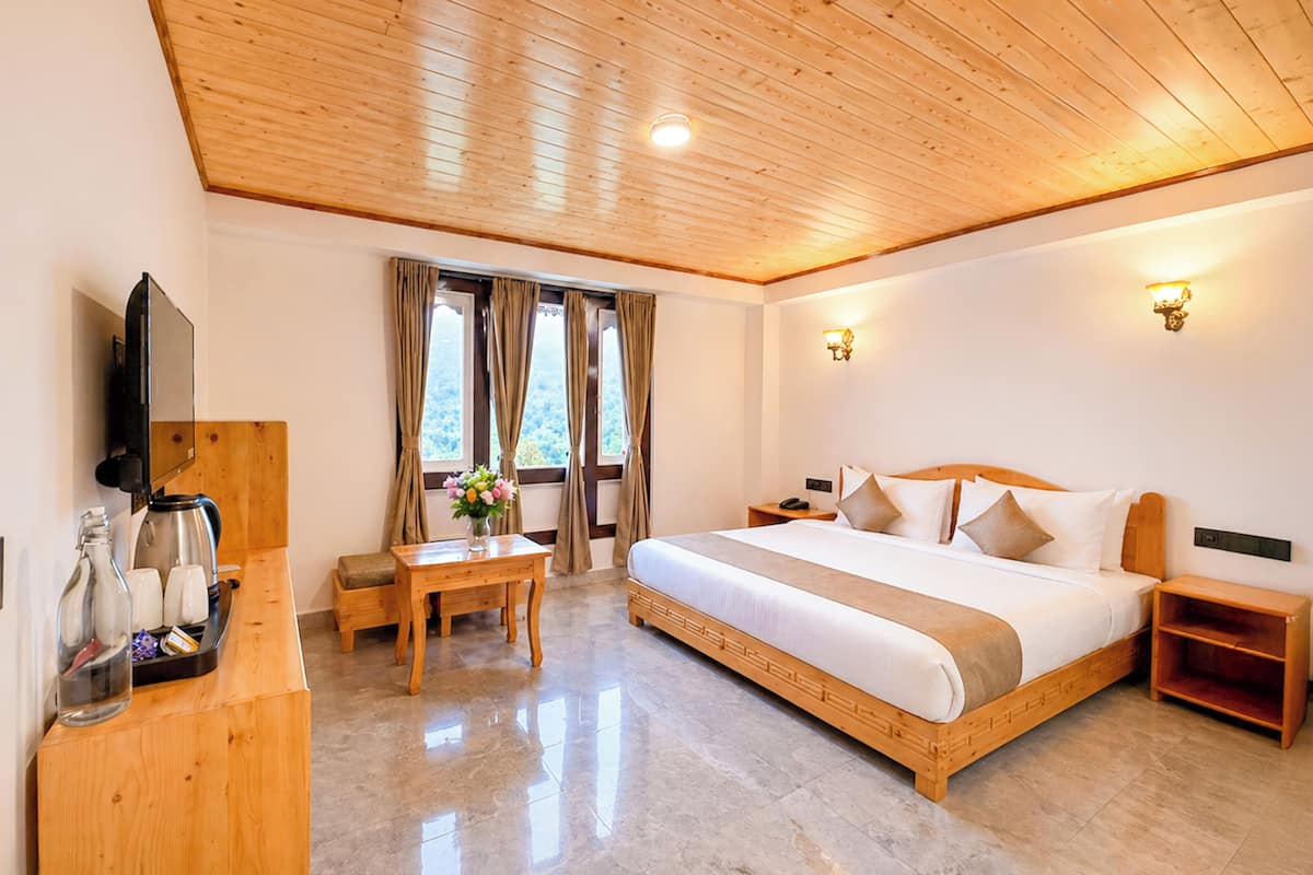 A hotel room with a wooden ceiling, a bed with white bedding, a wooden desk with a coffee maker, and a window with curtains.