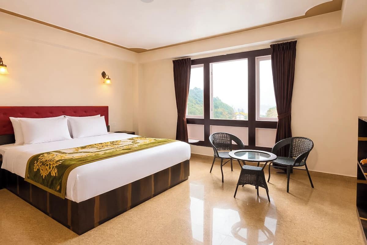 A hotel room with a large bed, a small round table, two chairs, and a view of the outdoors through a window.