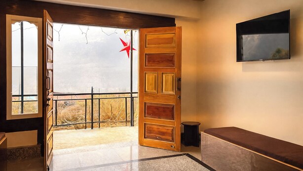 An open wooden door leading to a balcony with a metal railing, a bench, and a television mounted on the wall. - Sumitel Sonam Lachung (Chungthang)