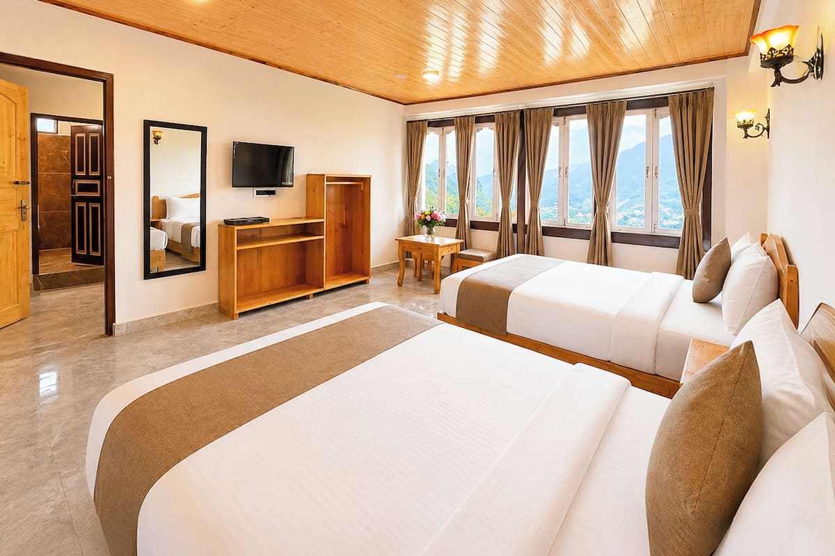 A hotel room with two beds, a desk, a TV, and a view of the mountains.