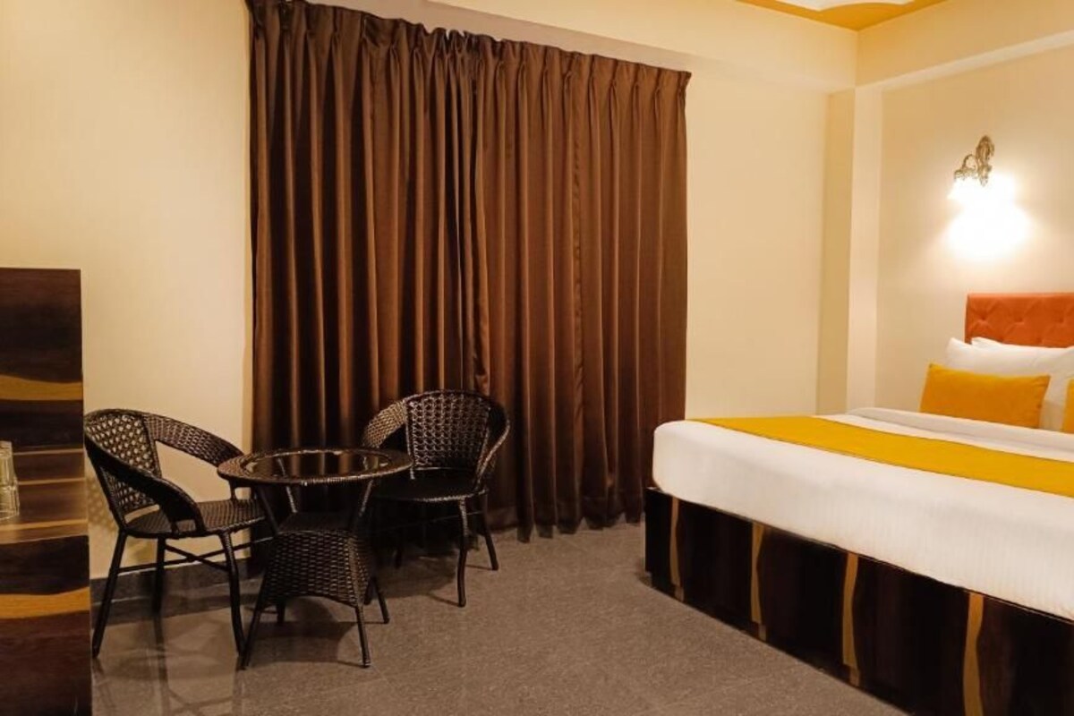 Una habitación de hotel con cama, una mesa y dos sillas, y una cortina.